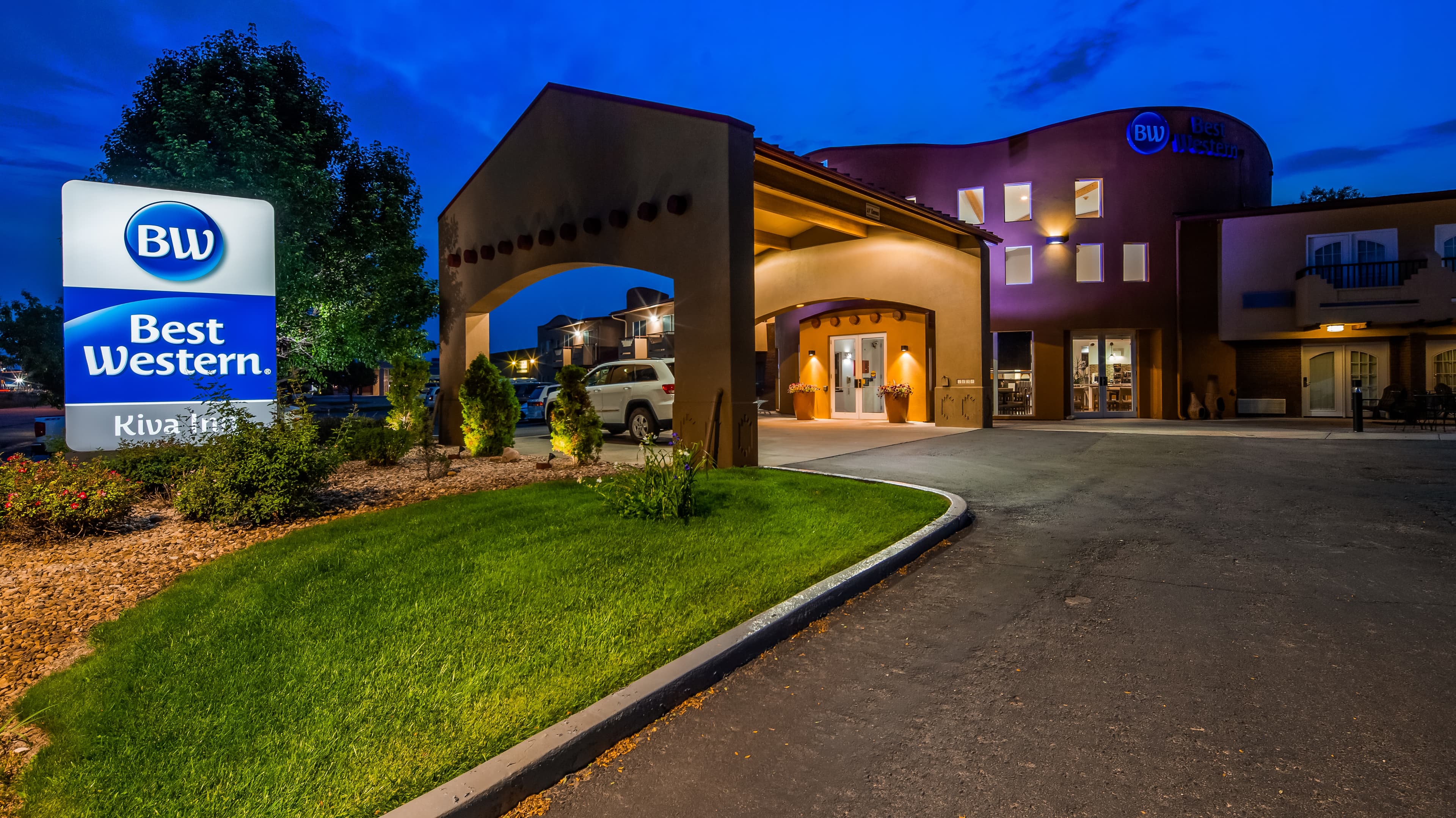 The exterior of the Best Western Kiva Inn in Fort Collins, Colorado at night; a building with Native-American inspired balconies, red-clay appearing facade and lush landscaping