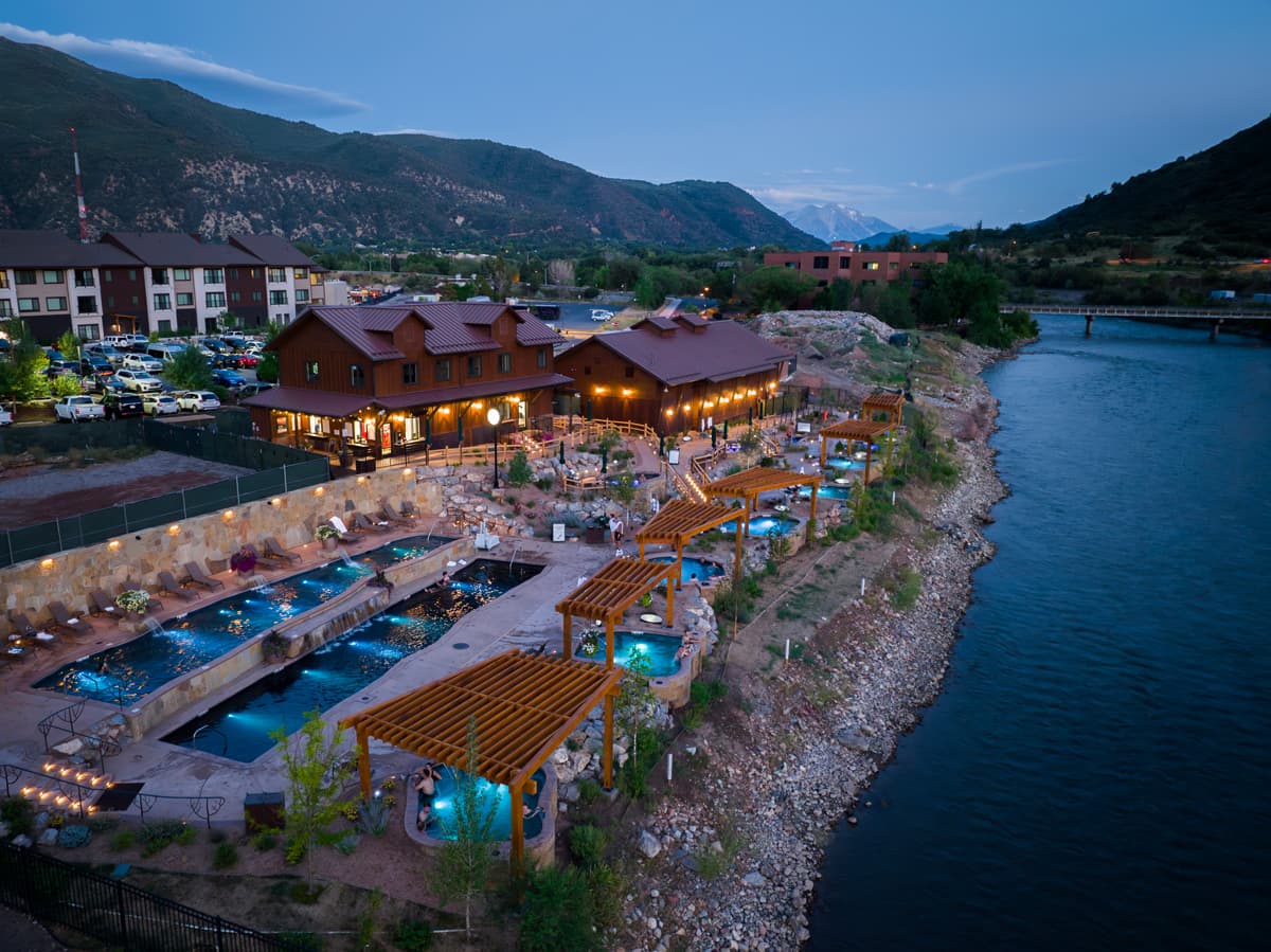 An aerial view of Iron Mountain Hot Springs with warm lights glowing and stunning teal-blue hot springs.