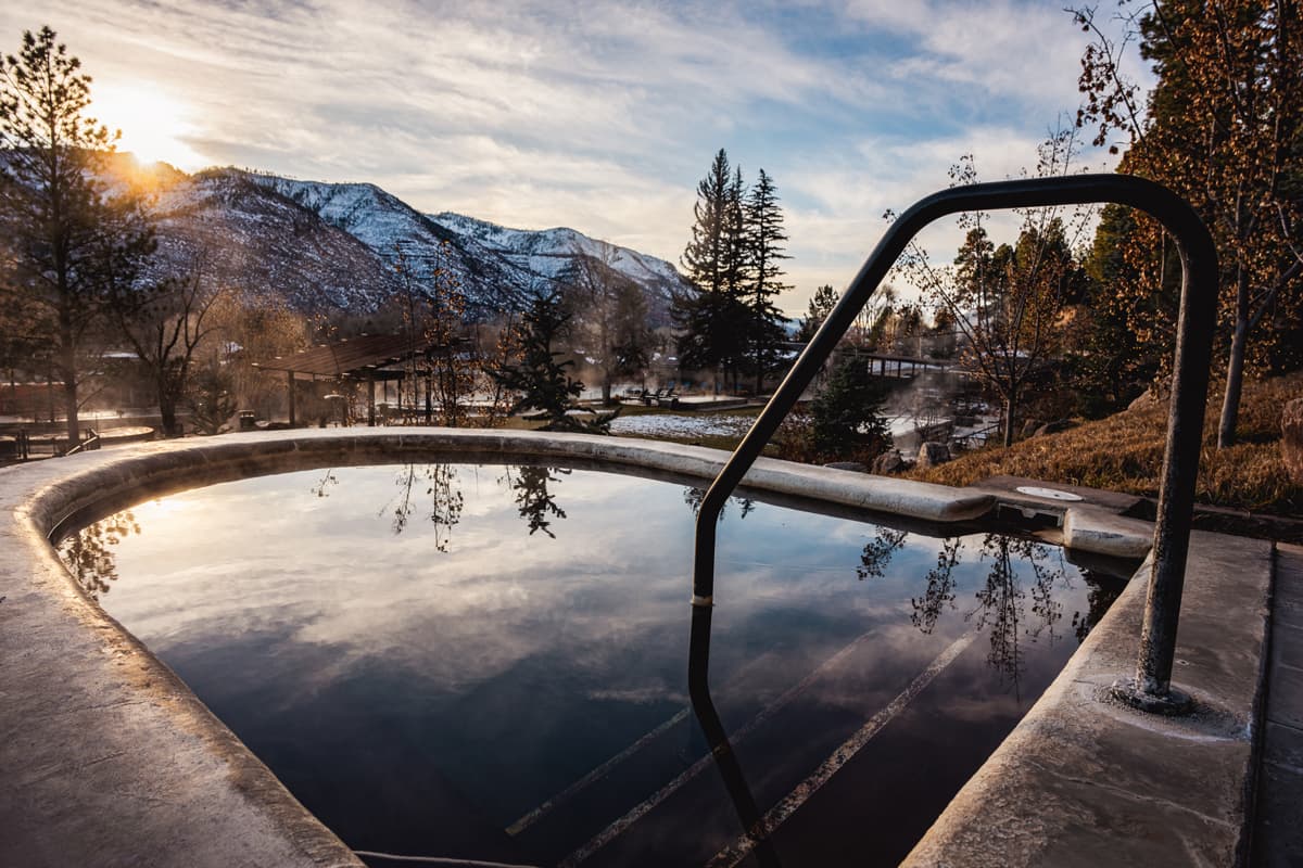 The sun crests snow-coated mountains and clouds are reflected in the still surface of a hot-springs pool at Durango Hot Springs resort + spa
