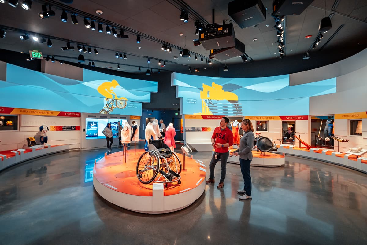 People in an open room look at paralympian wheelchairs at the US Olympic & Paralympic Museum Summer Games exhibit in Colorado Springs