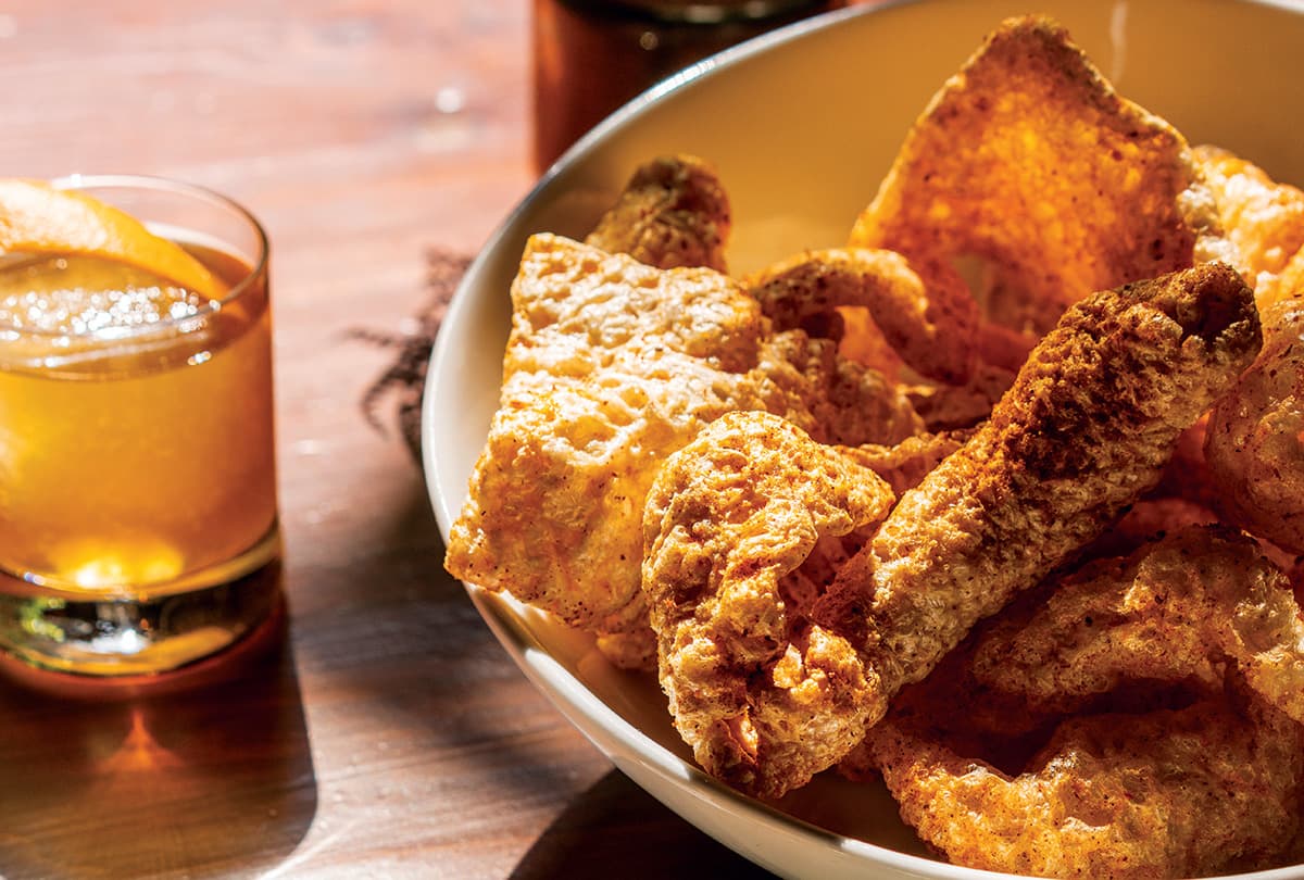 Chili-dusted pork rinds on a plate with a bright yellow cocktail