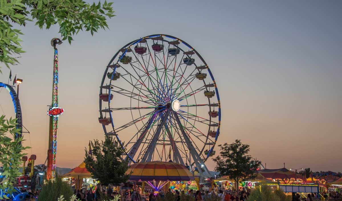 At dusk, a Ferris wheel and tall ride light up the night sky at the Boulder County Fair.