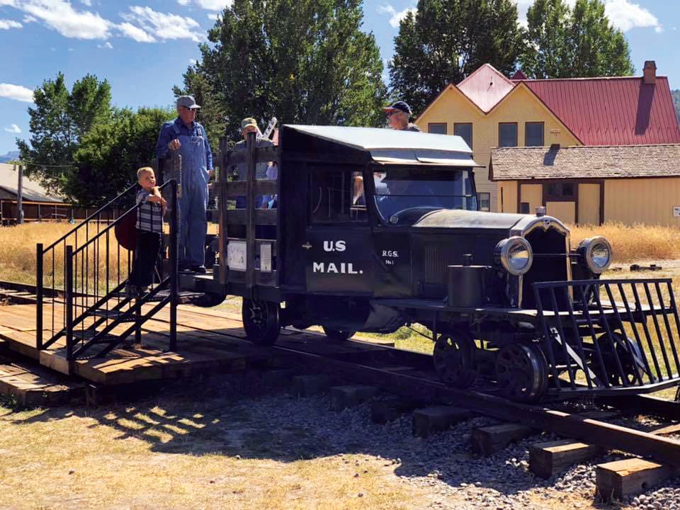 A child and several adults inspect an antique vehicle that appears to be equal parts train and automobile on a set of tracks at the Ridgway Railroad Museum in Colorado.