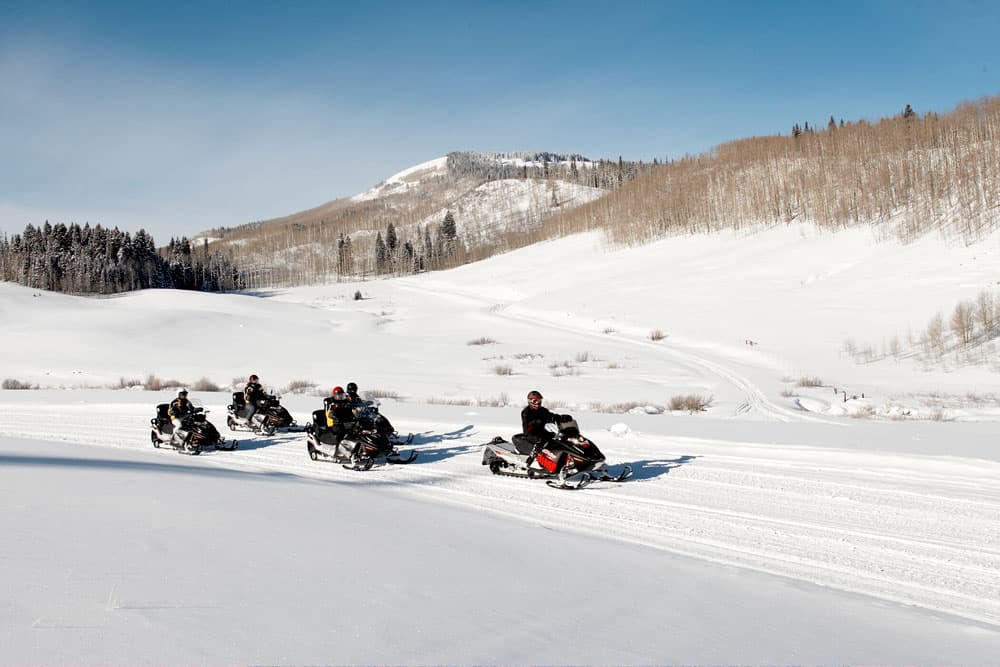 A group of snowmobiles ride across a mountain trail