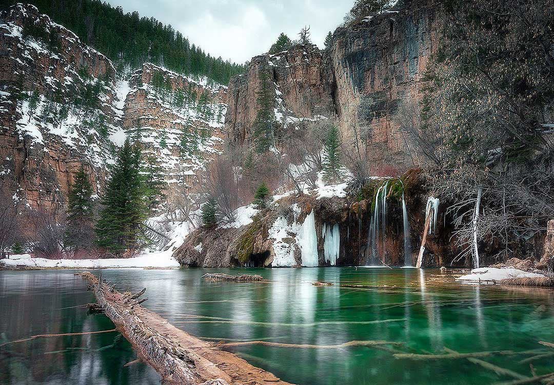A winter frost hangs over a placid lake near Glenwood Springs, Colorado. The nearby rock walls are covered in a light layer a snow and some waterfalls that feed the lake are frozen solid.