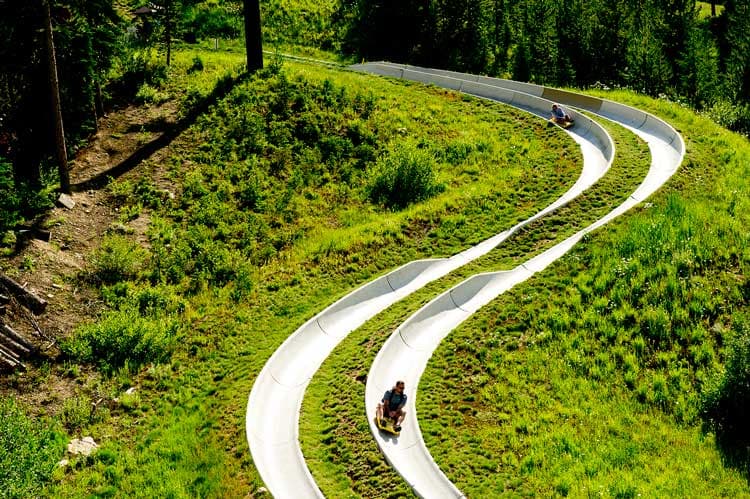 Two people slide on yellow mats down two twisting alpine slide at Winter Park Resort in Colorado.
