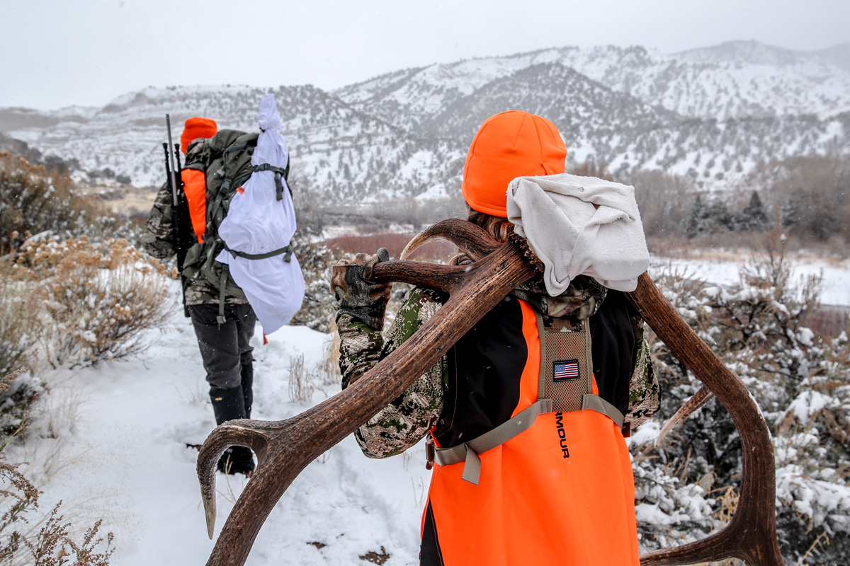Hunters in camo and orange vesets and hats pack their bounty out of the woods
