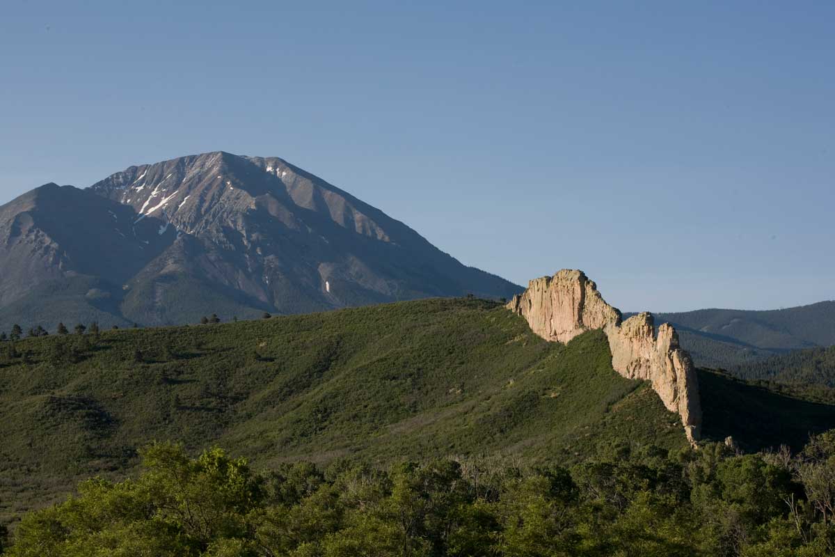 A rocky outcropping on a forested ridge stands in the looming shadow of the Spanish Peaks near La Veta, Colorado.
