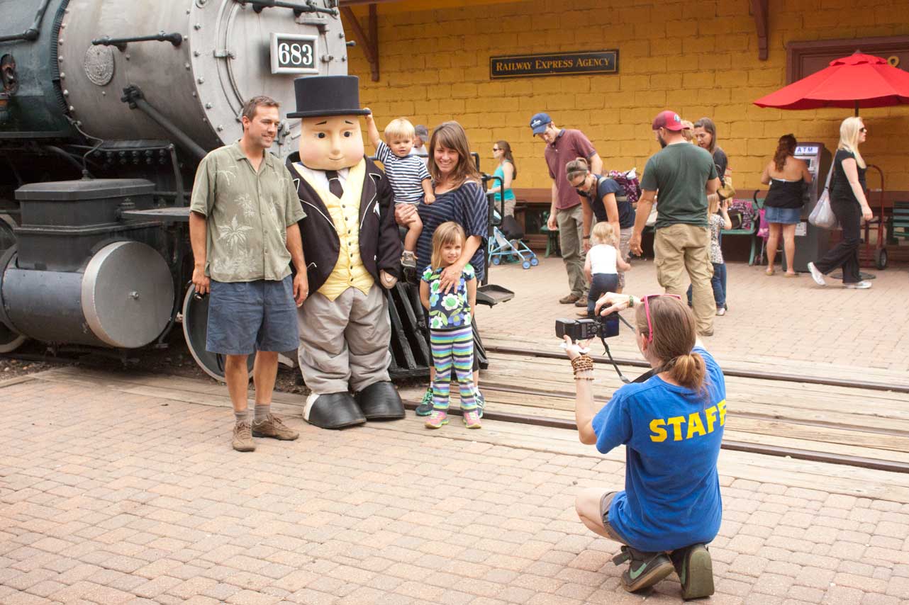 A family gets their picture taken at the Colorado Railroad Museum in Golden in front of a train and with a mascot dressed in a three-piece suit.