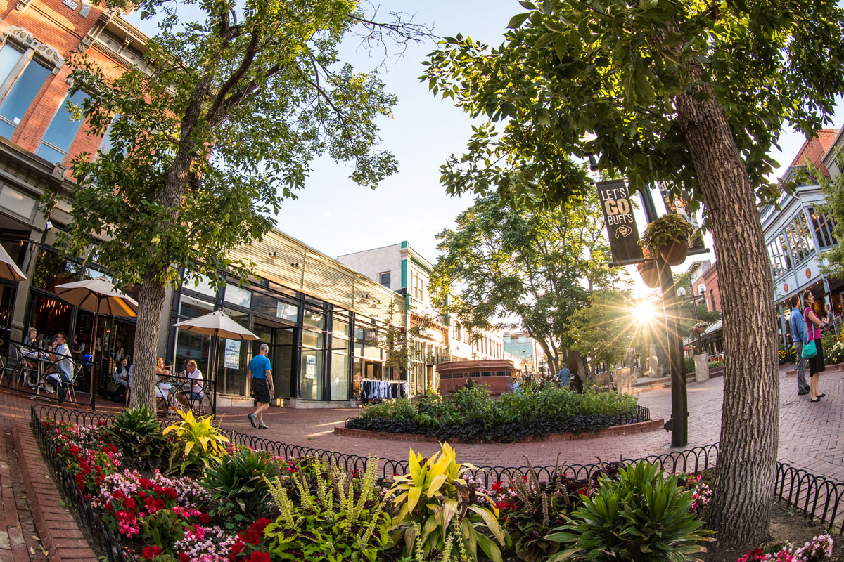 In summer, downtown Boulder's Pearl Street is filled with trees covered in green leaves, excited shoppers and vibrant flowers in garden beds.