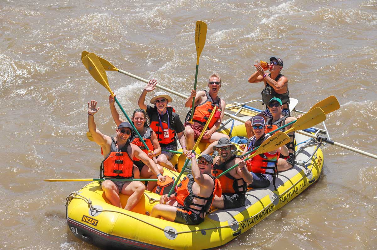 Participants hold their paddles up while sitting on a yellow raft during Big Gay Raft Trip in Glenwood Springs