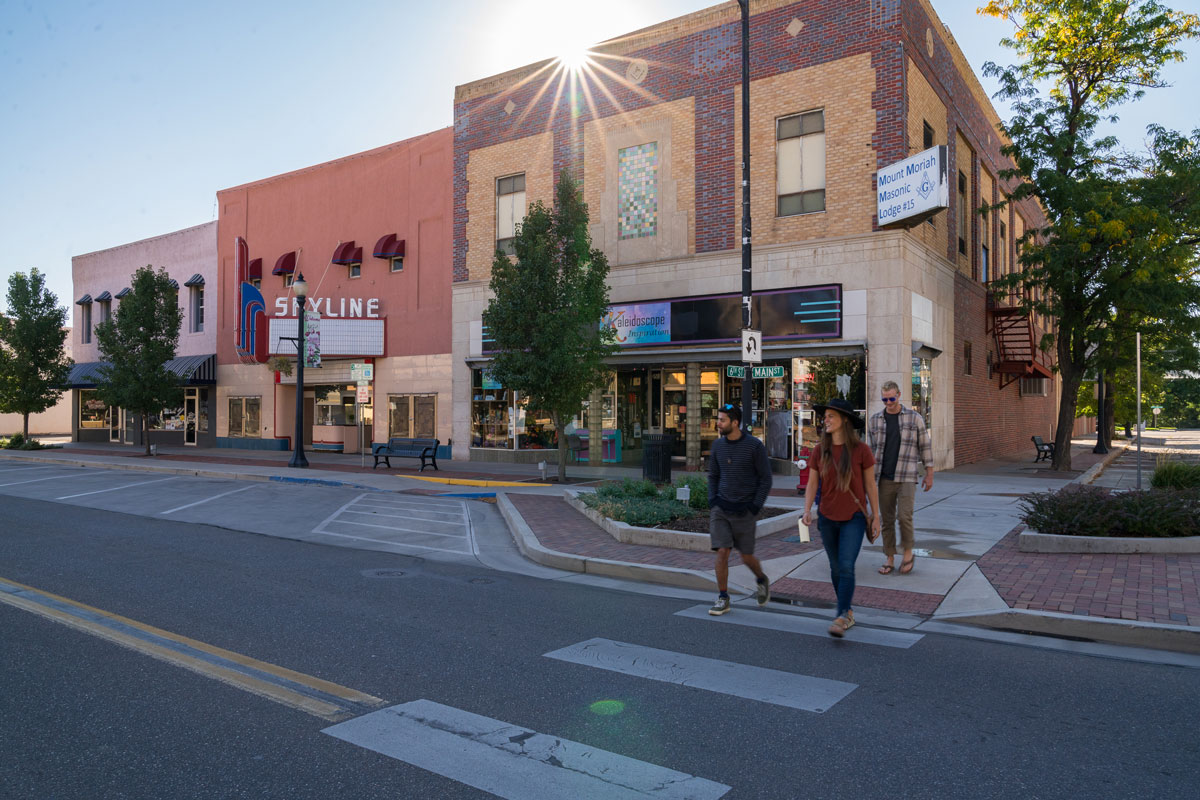A group of happy friends walks across the street amongst the shops and the Skyline Theatre in downtown Cañon City.