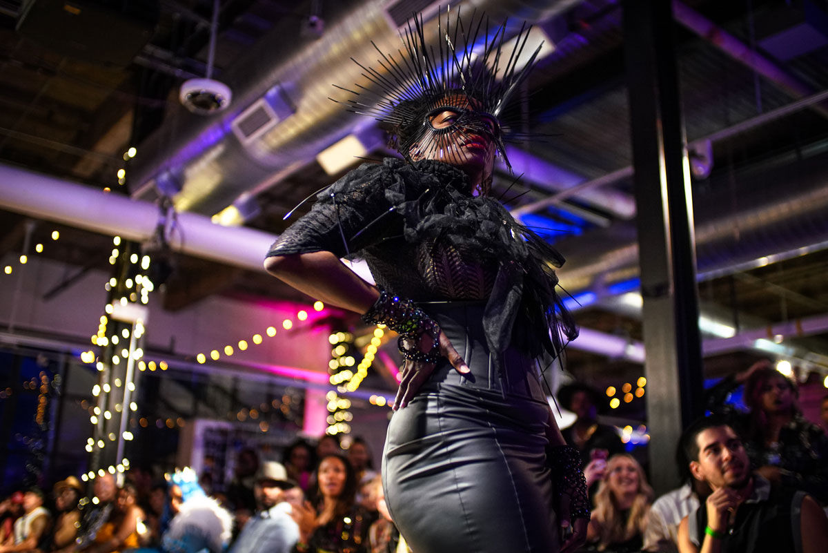 A person poses in an all-black outfit, complete with ruffles, beaded jewelry, a leather skirt and a pointy black eye mask in Colorado.