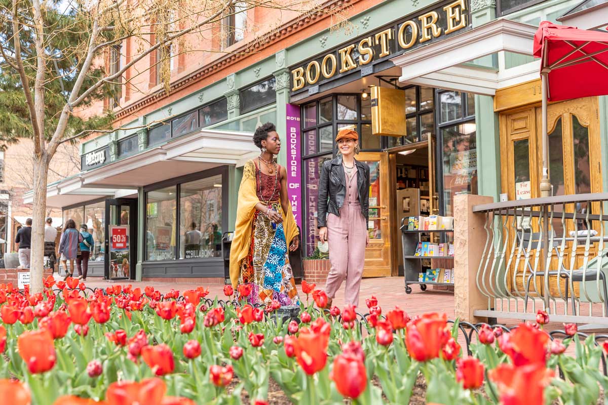 Two people walk by the Boulder Bookstore in a pedestrian area; on their otherside is a flower box filled with red tulips