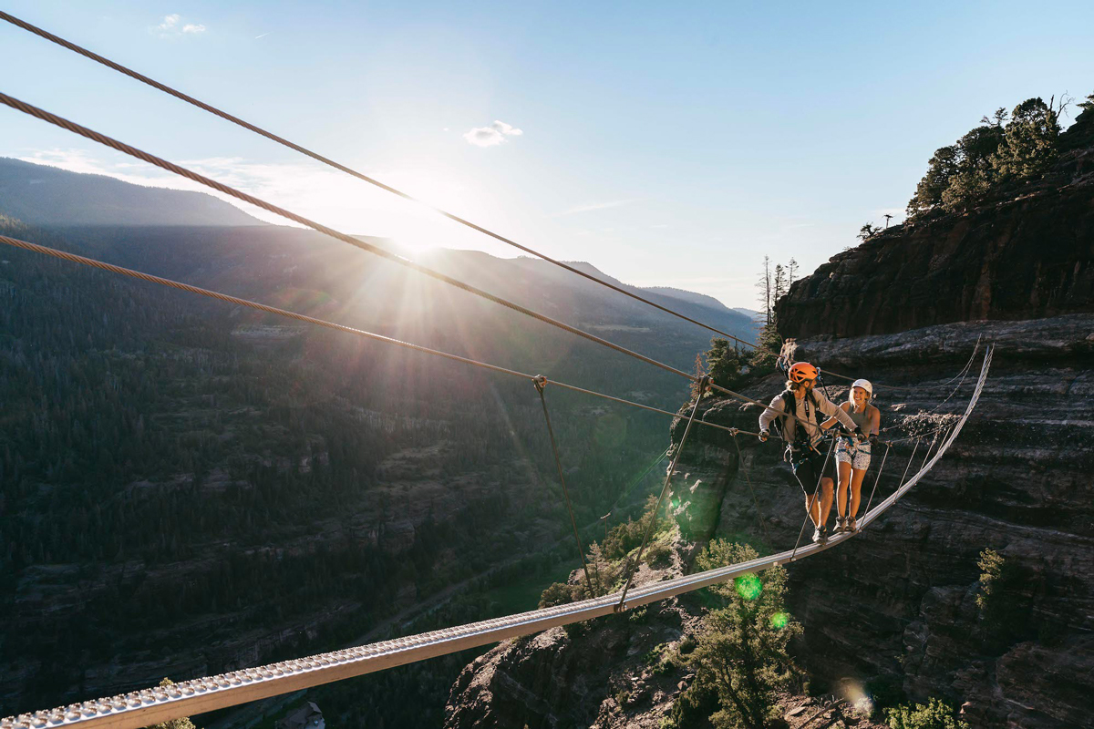 Two people make their way across a canyon on a narrow catwalk while traversing the Gold Mountain Via Ferrata in Ouray, Colorodo