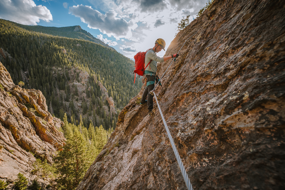 A person climbs a cliff face using cables in Estes Park, Colorado.