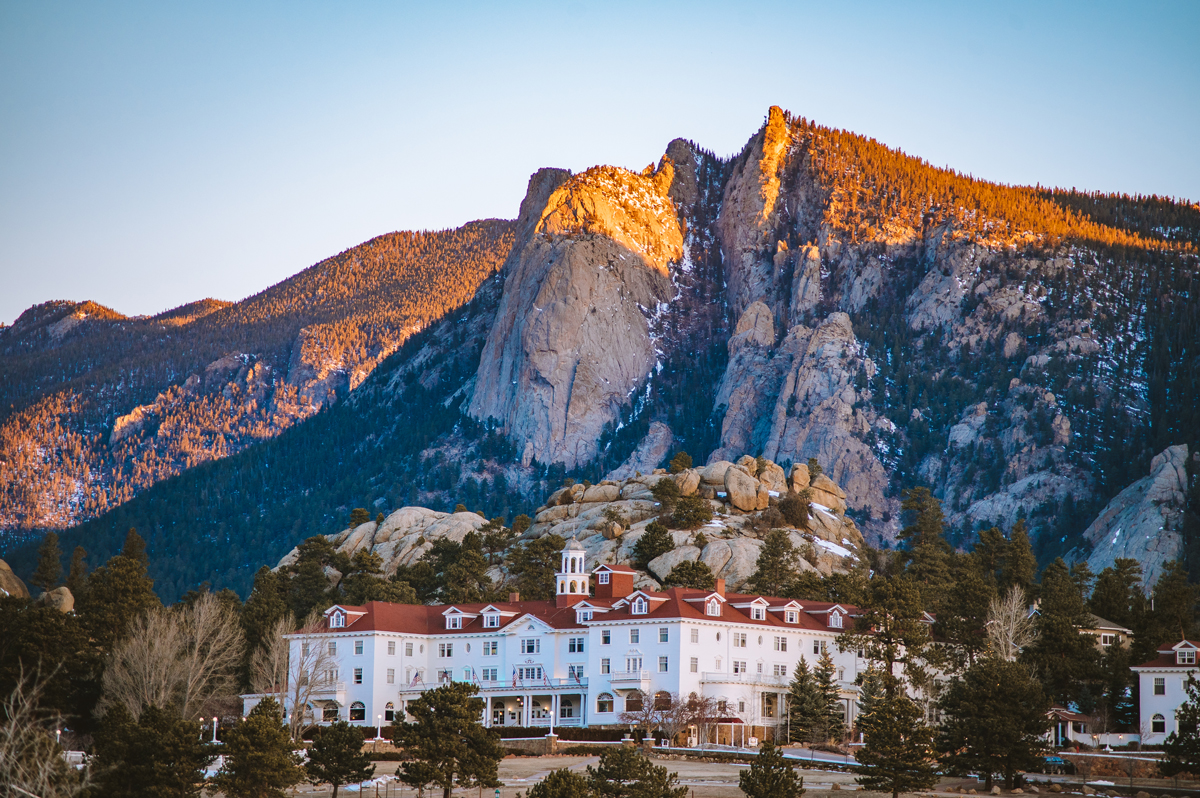 The Stanley Hotel in Estes Park, Colorado — a beautiful white historical hotel with a red roof and mountains rising in the background.