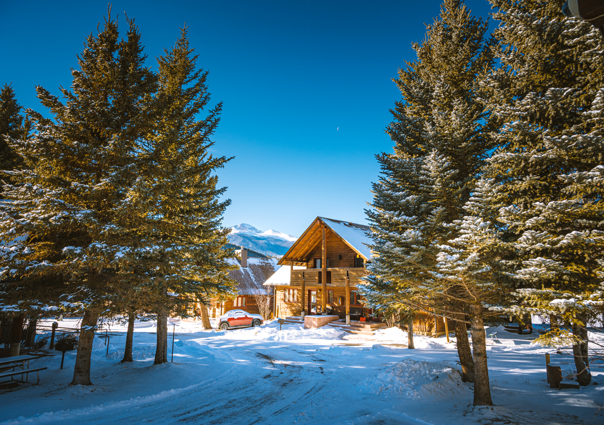 A snow-flocked cabin flanked by evergreens and a mountain backdrop delights at Rams Horn Village Resort in Estes Park, Colorado. 
