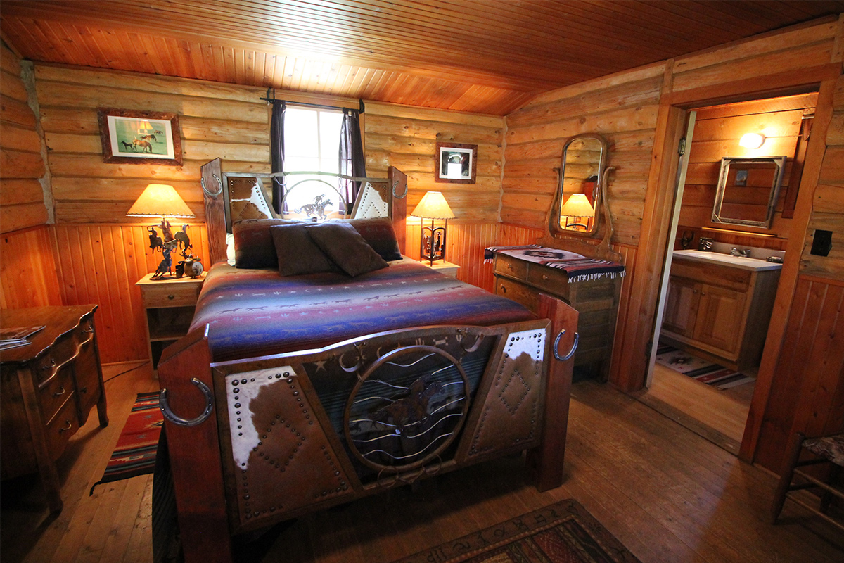 A bedroom in a guest cabin at Bar Lazy J Guest Ranch features an ornate headboard complete with cow hide and horseshoes.