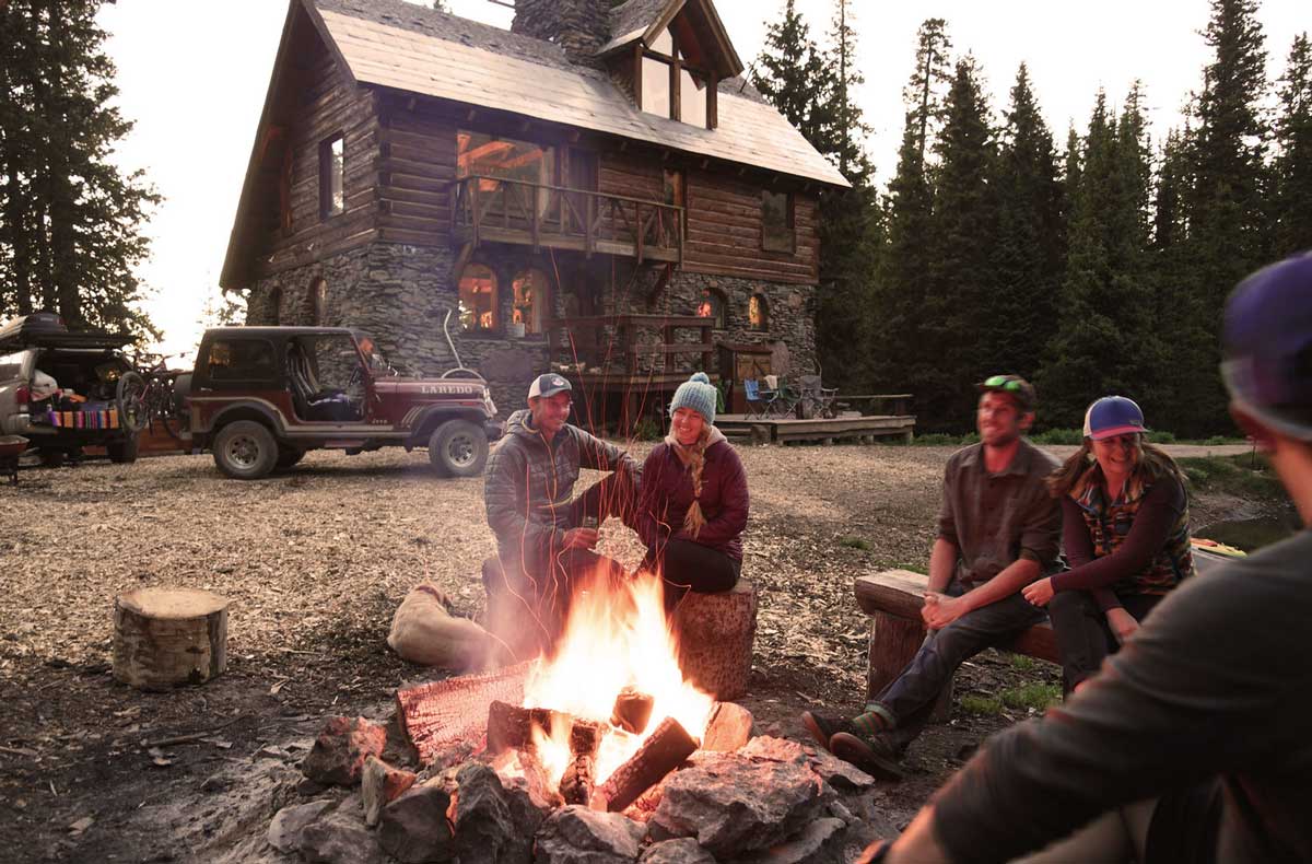 A group of people sit around a campfire with The Observatory at Alta Lakes in the background