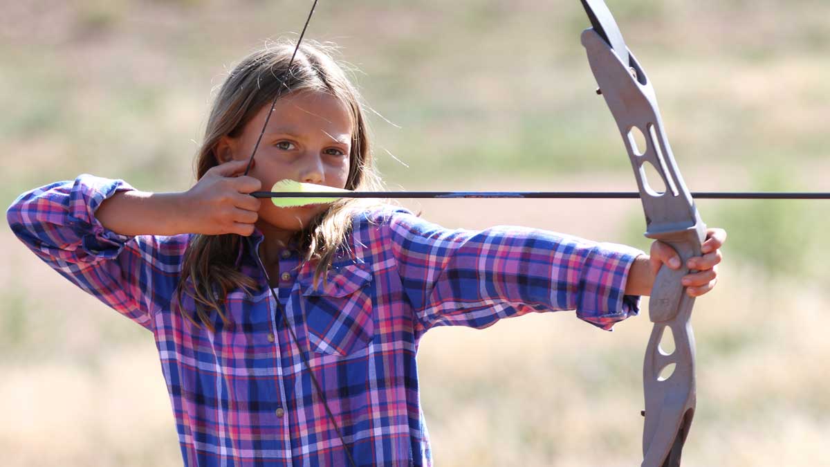 A child prepares to shoot an arrow at a target while visiting Black Mountain Ranch
