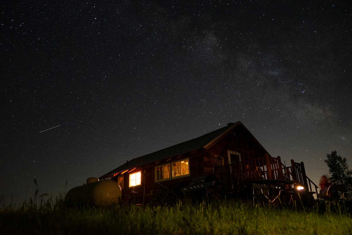 Colorado Cabin Escape at night. The lights of the cabin are on. Stars twinkle in the night sky behind the cabin.