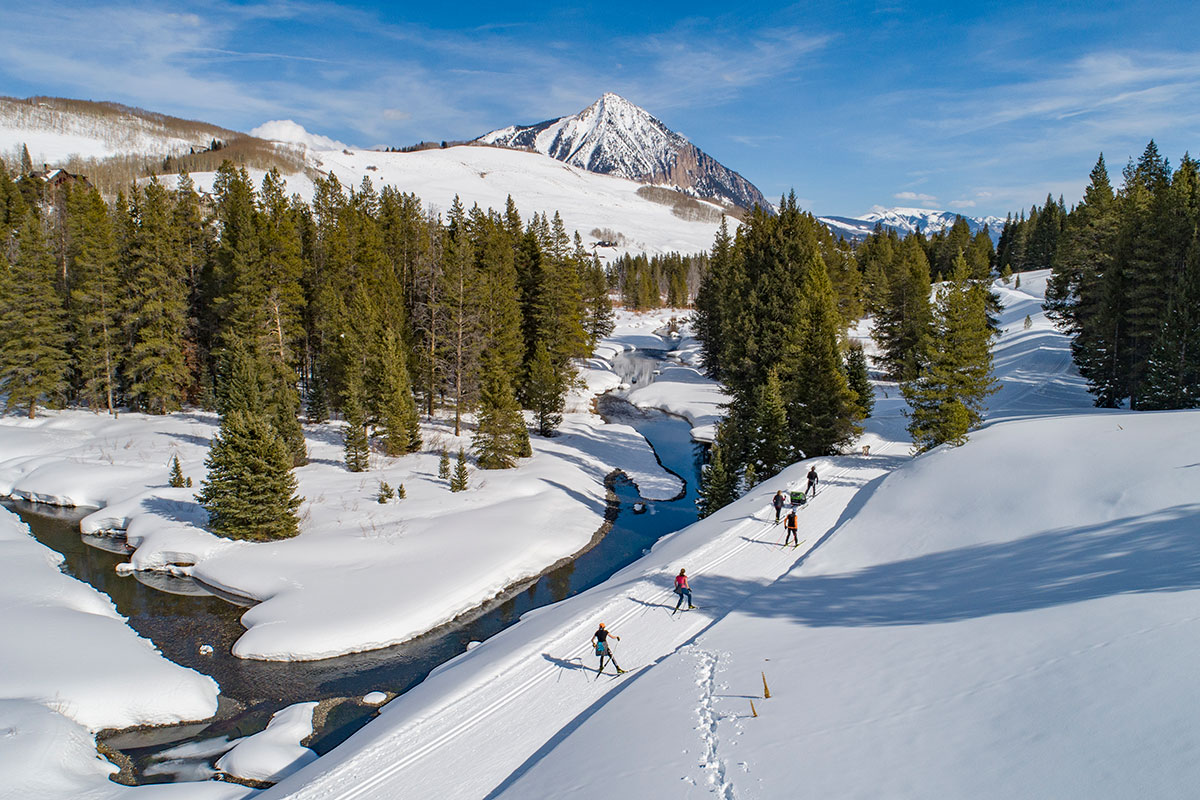 A group of cross-country skiers along a river with a tall mountain in the background