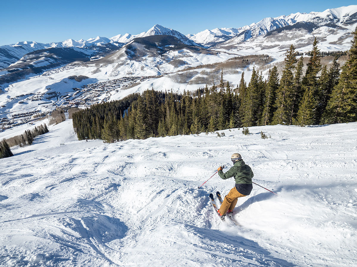 Aerial view from behind of a skier navigating a bumpy ski run with mountain peaks in the distance