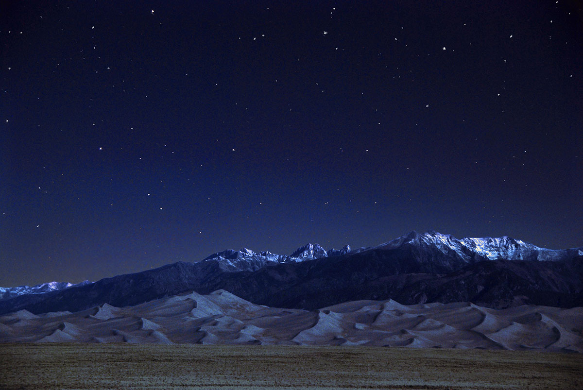 Night sky with stars above snowy mountains and sand dunes