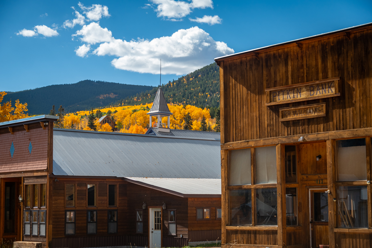 Bright gold patches of aspen leaves stand out against evergreens behind the Old West buildings in Pitkin, Colorado.