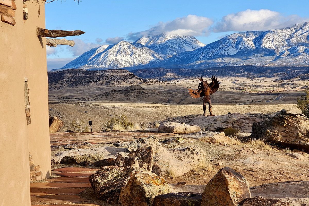 A statue of an Eagle Dancer poses by the Sky Kiva building with stunning mountains in the background at Canyon of the Ancients Guest Ranch.