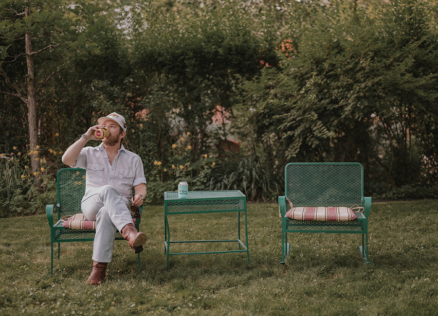 A guests sits on a wire patio chair and relaxes in the verdant garden at Gable House B&B in Durango, Colorado.