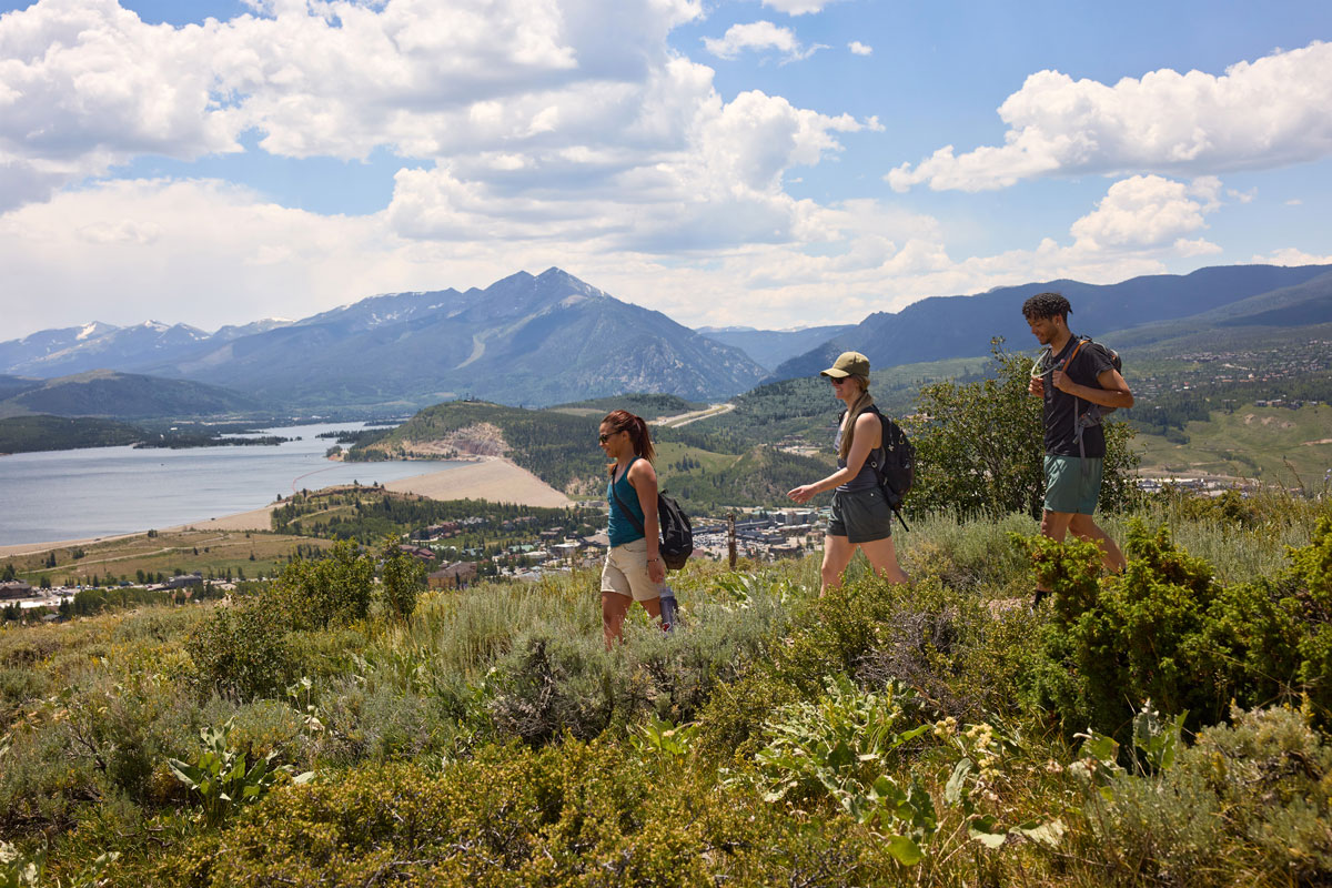 Hiking the hills of the Ptarmigan Trail beneath a blue sky with a mountain backdrop.