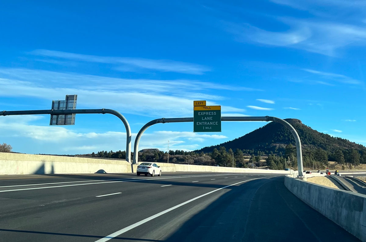 A white car driving smoothly along the Colorado Express Lane, featuring a mountain in the background.