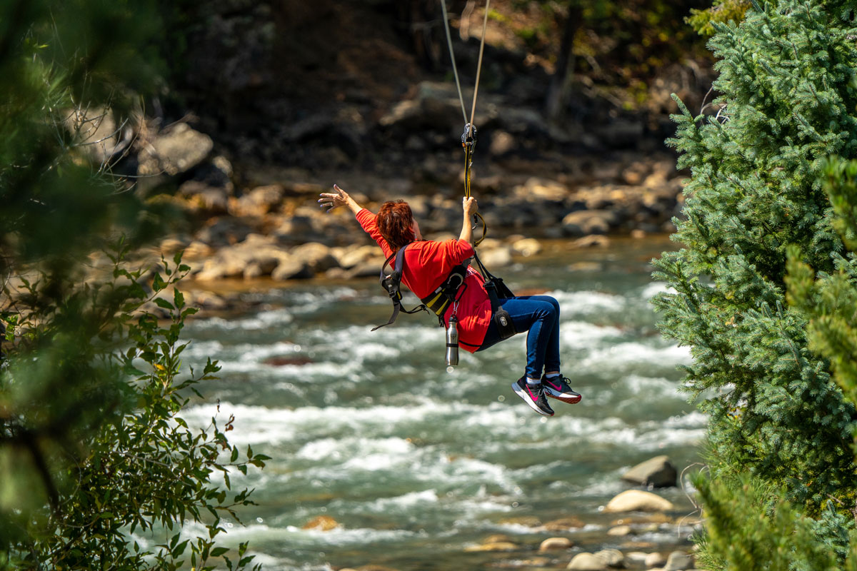 A woman ziplining above the rushing Animas River, surrounded by trees in Colorado.