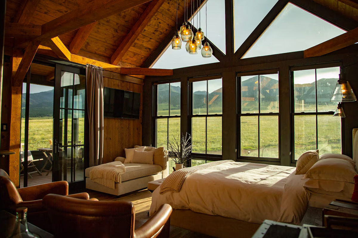 From the bedroom at the Three Peaks Ranch near Westcliffe, Colorado, a comfy bed and cream chaise make perfect spots for lounging and gazing out the window.