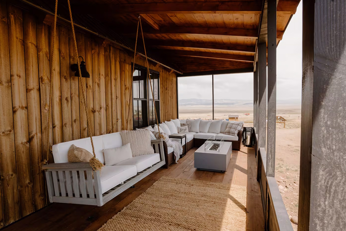 A screened-in porch at a cabin on Three Peaks Ranch in Colorado, features a cozy swing and a plush sectional.