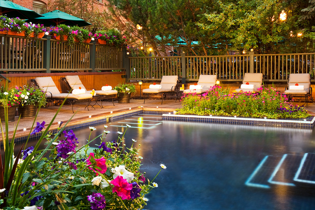 The pool area at the Hotel Jerome in Aspen, Colorado, is lavish with comfortable tan chaises and abundant blooming flowers.