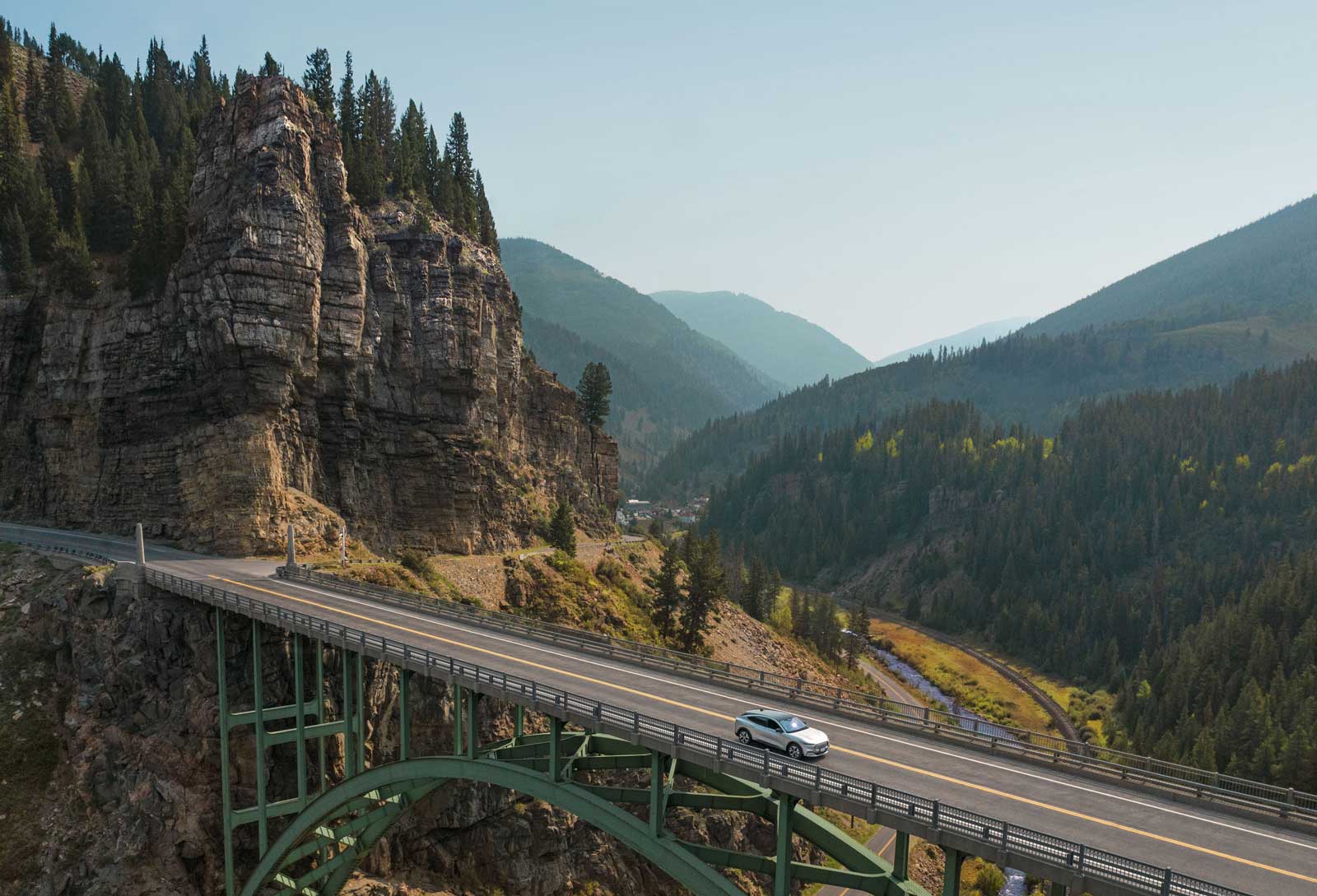 A car drives over a green metal bridge surrounded by jagged canyon walls