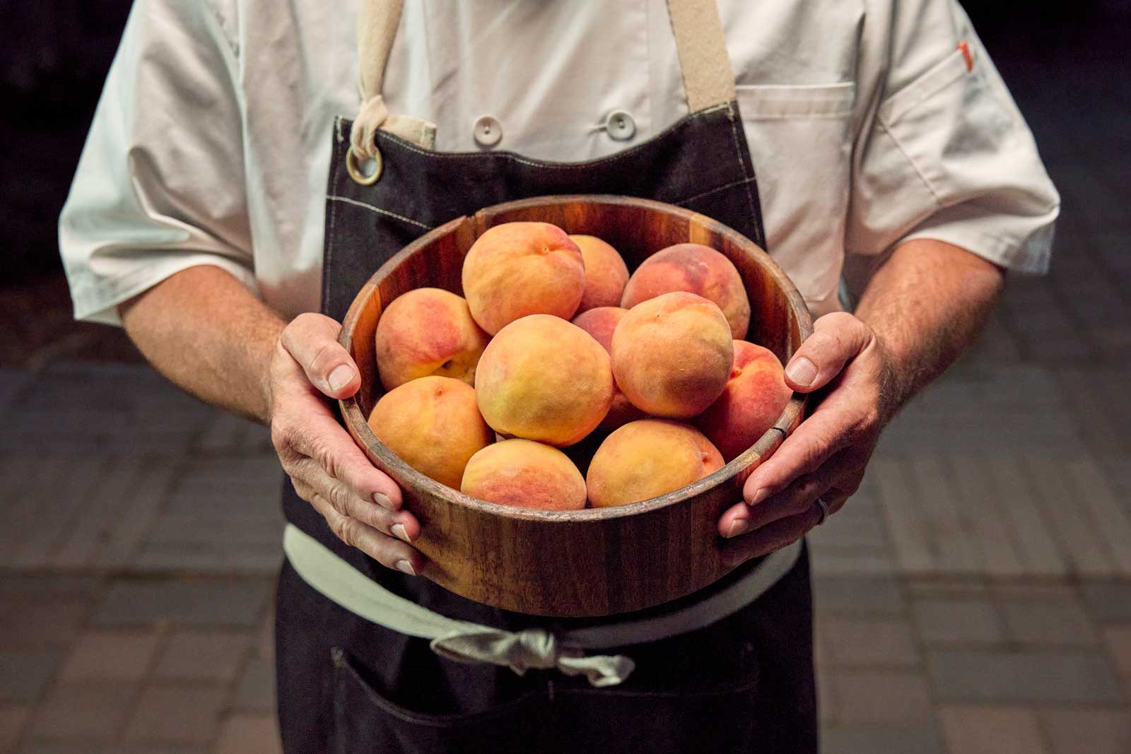 A chef holds a basket of ripe peaches