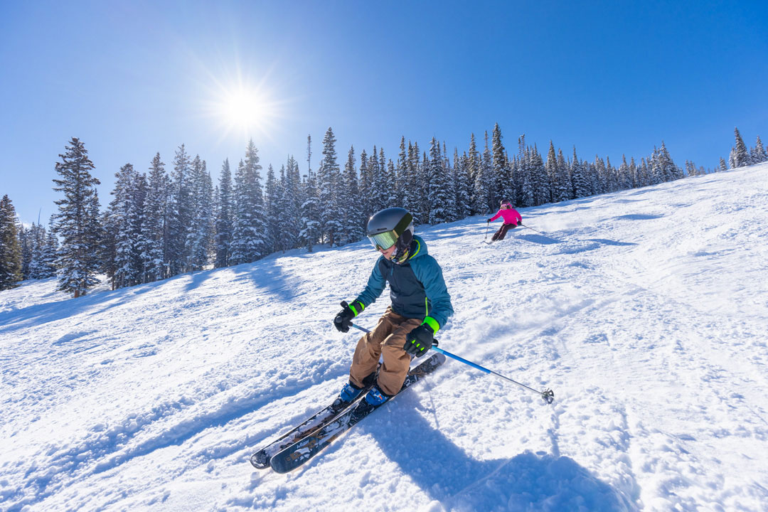 A skier in a helmet safely navigates the snowy slopes under the Colorado sun