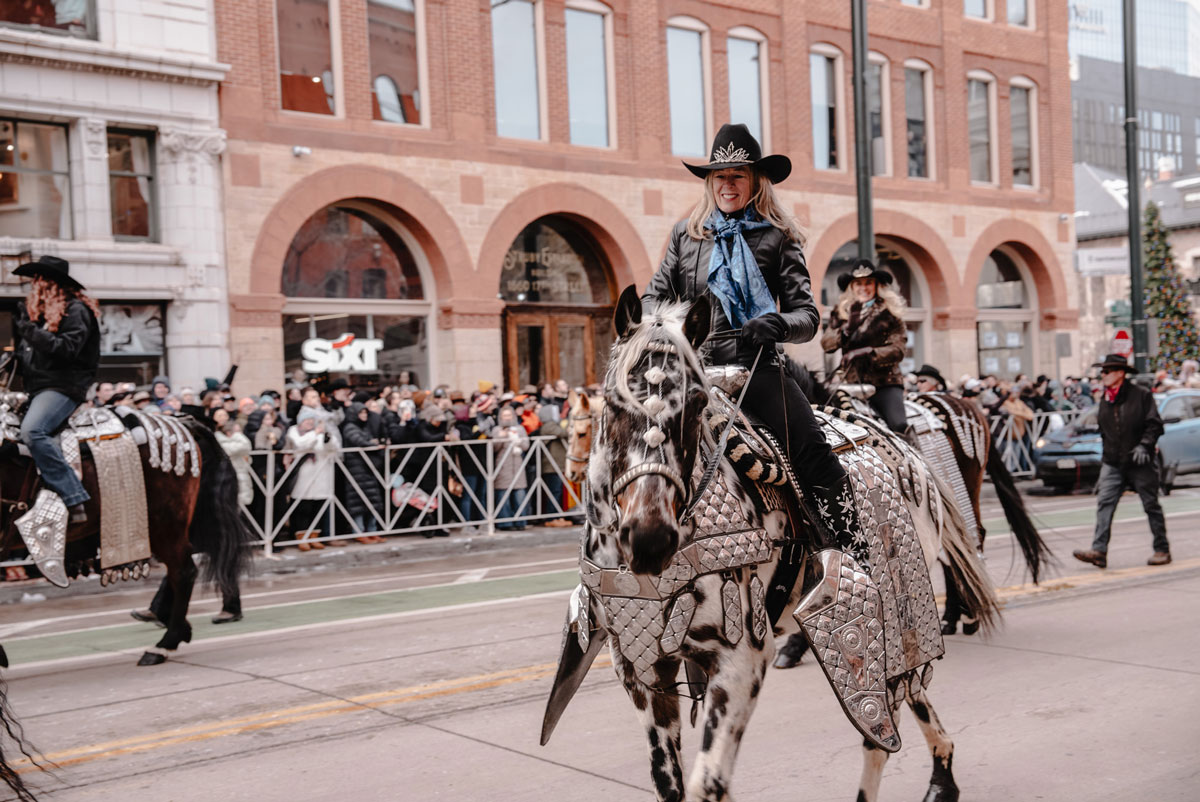 A woman on a horse rides down a street in Dnever as part of the National Western Stock Show Parade