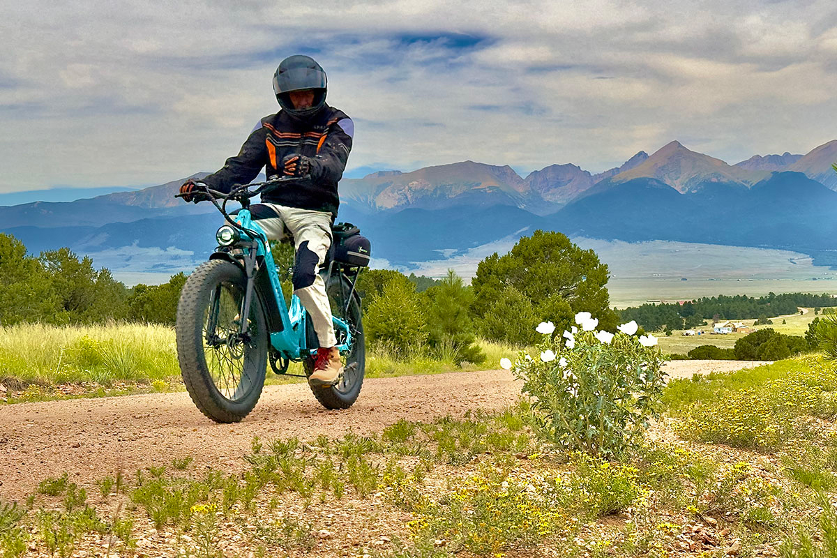 A cyclist on a fat bike rides down a trail in Westcliffe, Colorado with the mountains rising in the background.