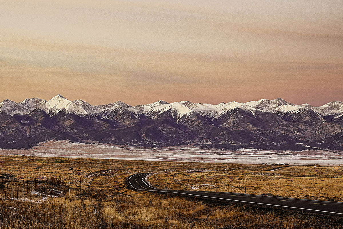 Sunset glow over a scenic road with snow-capped mountains in the background in Colorado.