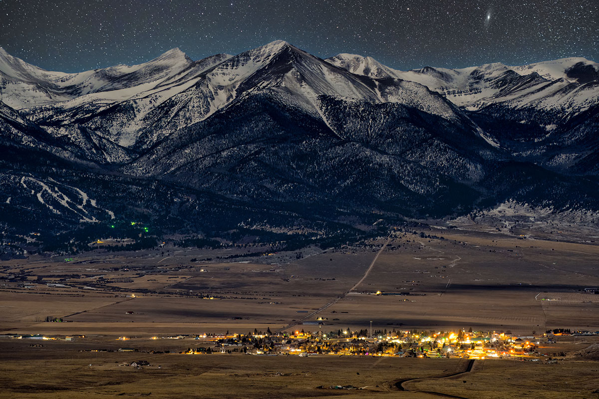 Far away view of the town of Silver Cliff at night with warm lights coming out from the town and a mountain background.