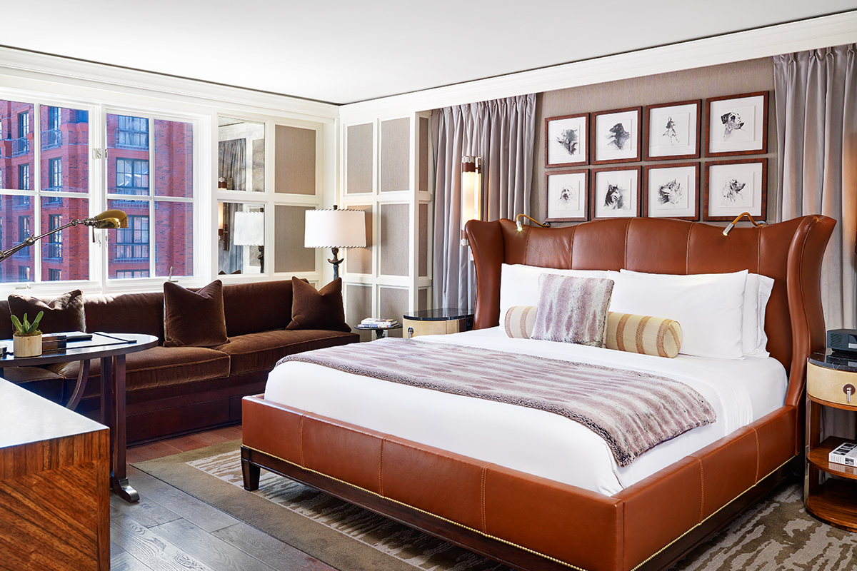 A guest room at the St. Regis Aspen Resort features a lavish bedroom with a stylish leather headboard, a velvety couch and wood floors.