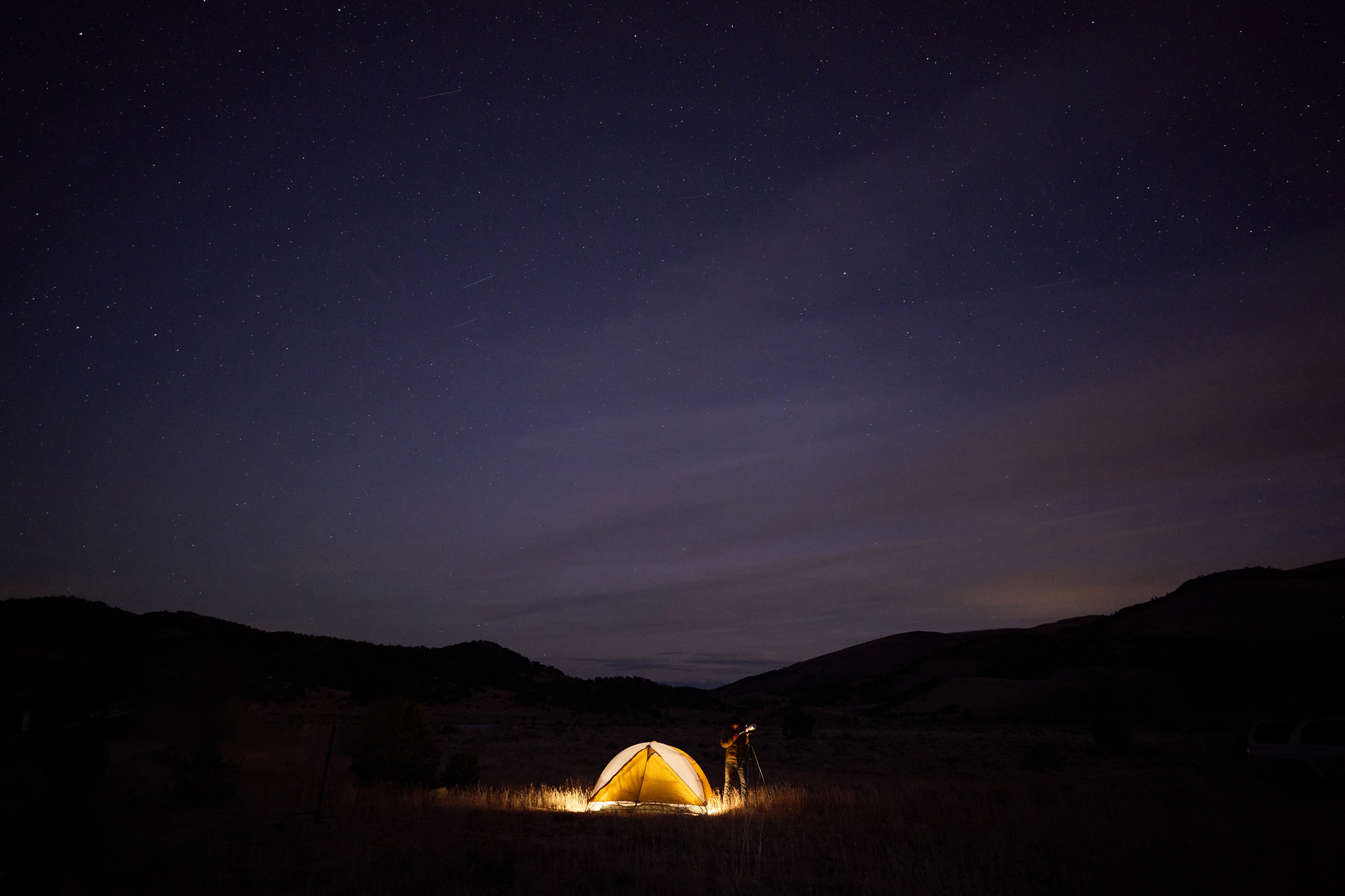 A camper by his tent uses a telescope to look at Colorado's starry sky. 