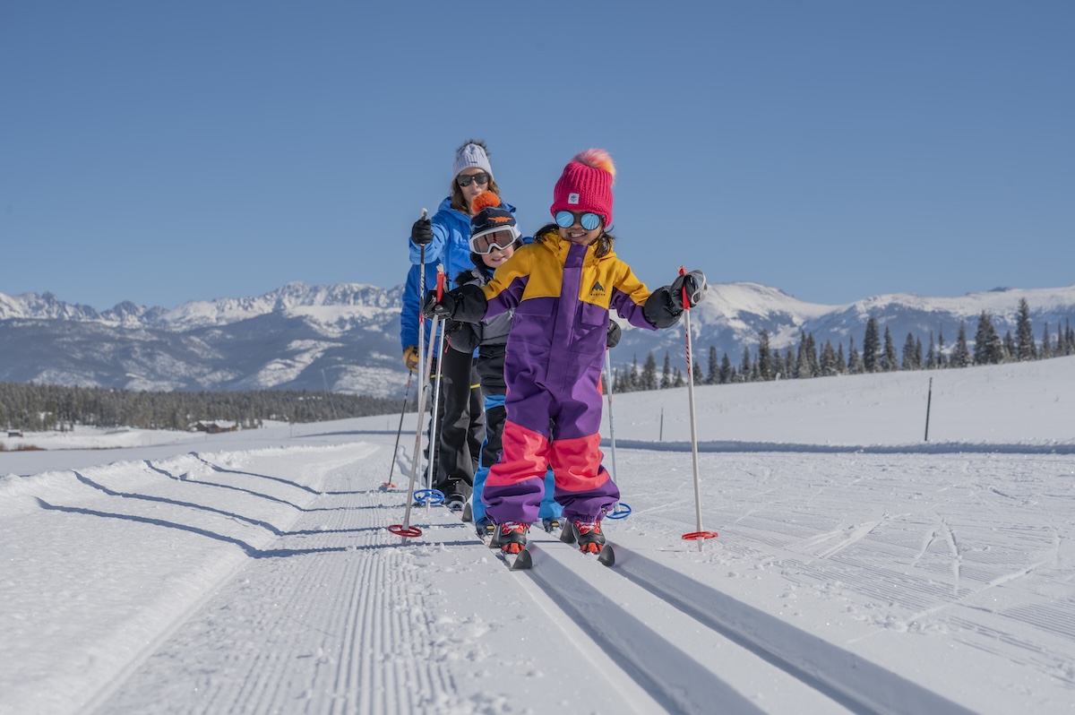 A family wearing bright winter coats and Nordic skiing directly towards the frame on powdery white snow in Granby, Colorado.
