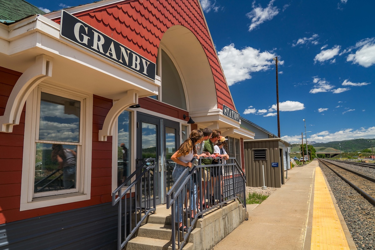 People looking out at railroad tracks outside the red Granby Station in Granby, Colorado.