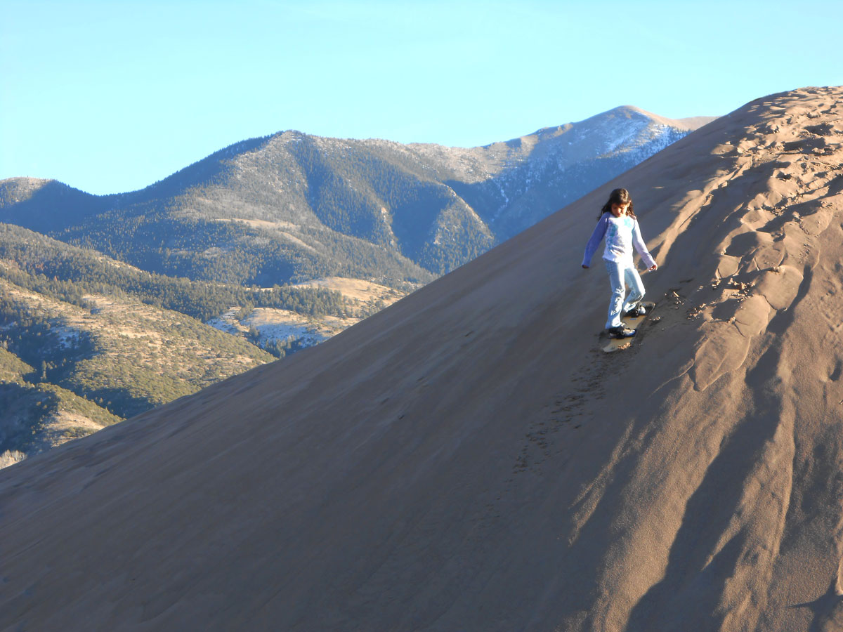 A girl rides a snowboard down a dune at Great Sand Dunes National Park